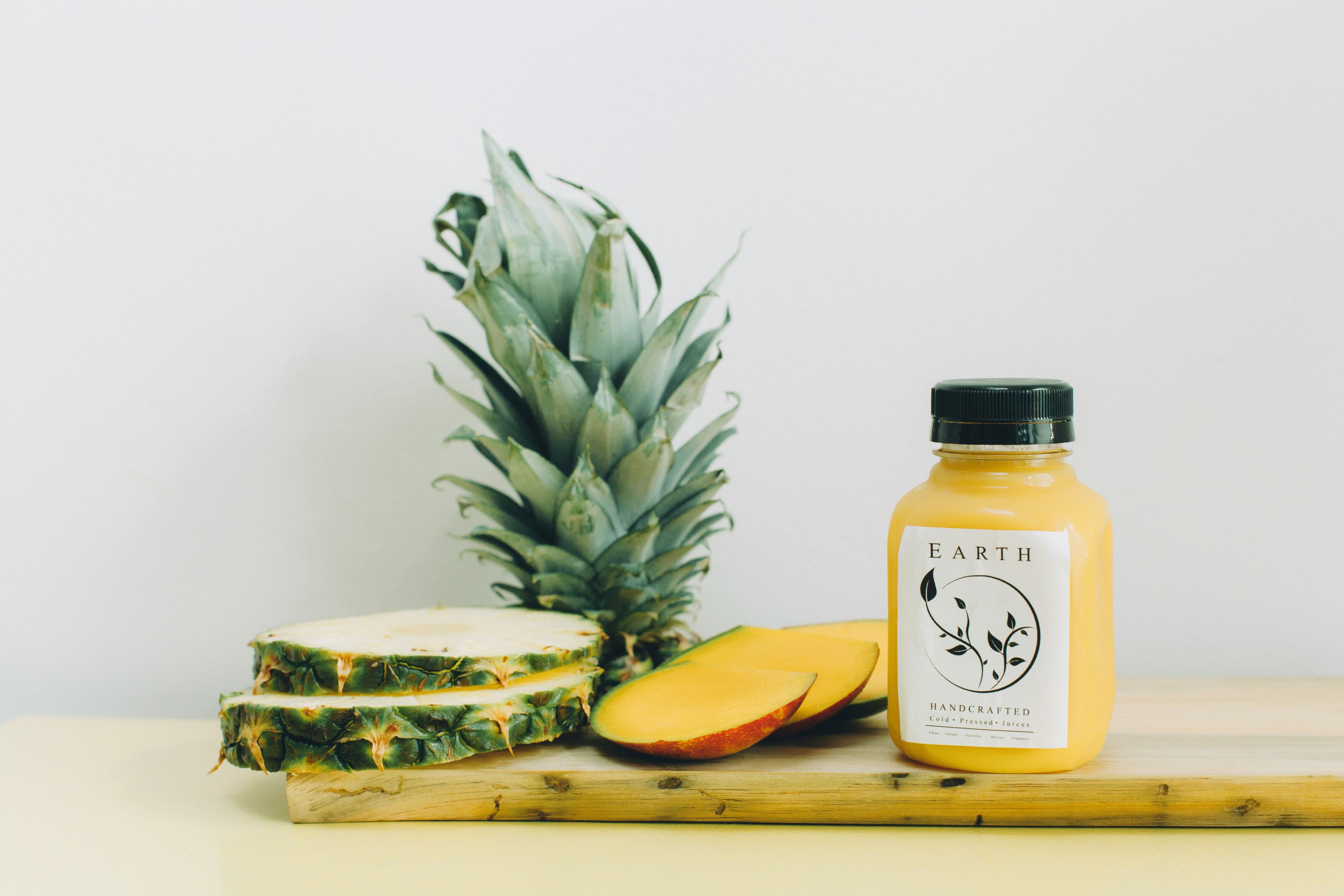 Earth Mango Cold Pressed Juice bottle with vibrant mango graphics on a wooden table, showcasing fresh, natural ingredients.