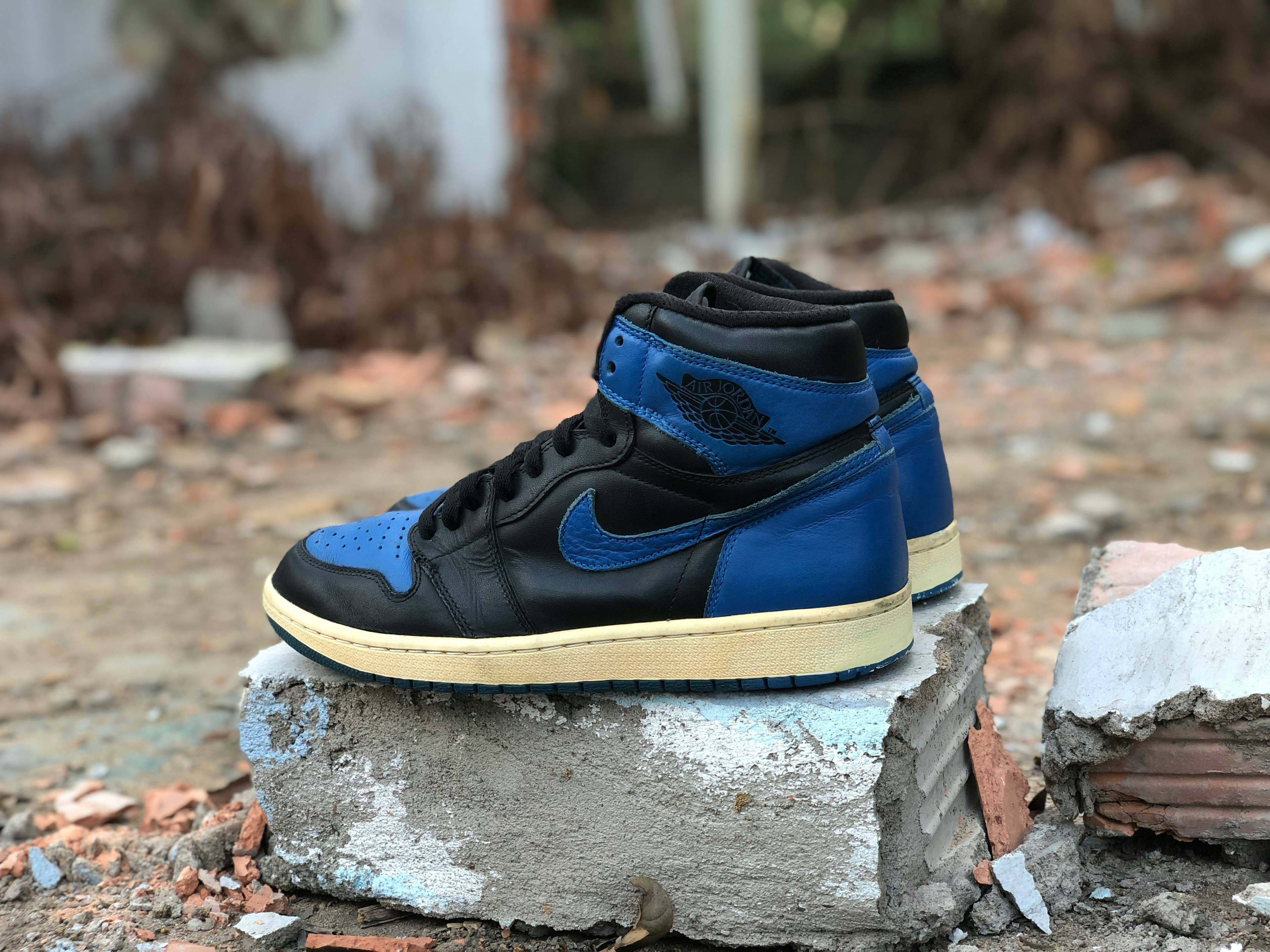 Blue and black high-top sneakers with Nike logo on concrete block, outdoors with a blurred background.